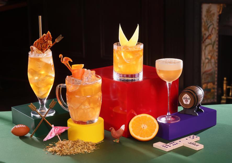 Four Greene King Brewery "casktails" on colorful pedestals surrounded by oranges, hops, and novelty items.