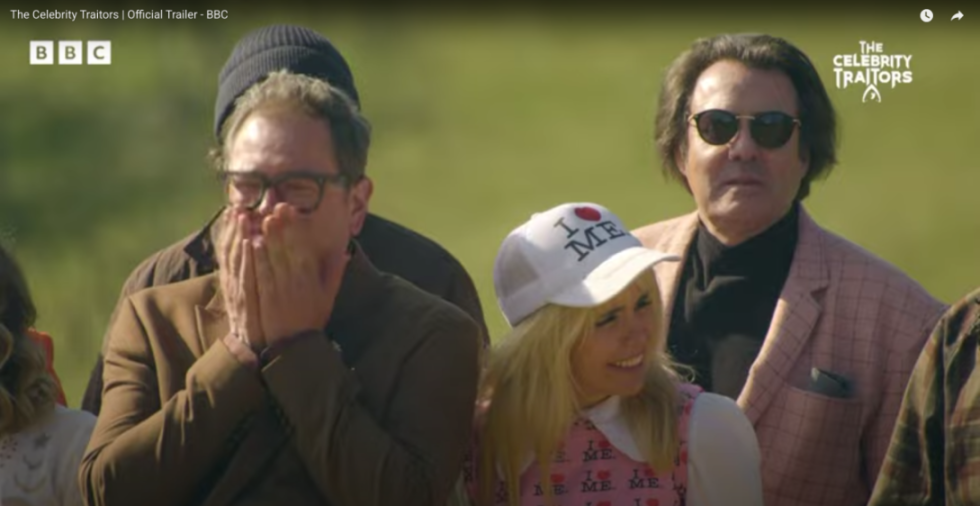 A man with glasses covering his mouth, a blonde woman in an "I Heart Me" hat, and a man in sunglasses with a pink plaid jacket, from "The Celebrity Traitors."