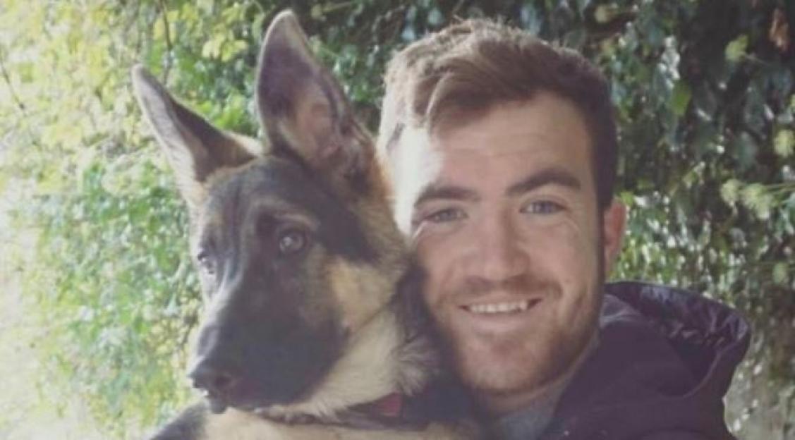 A man smiling and holding a German Shepherd puppy.