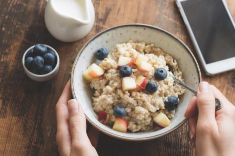 A woman eating a bowl of oatmeal with blueberries and peaches for breakfast.