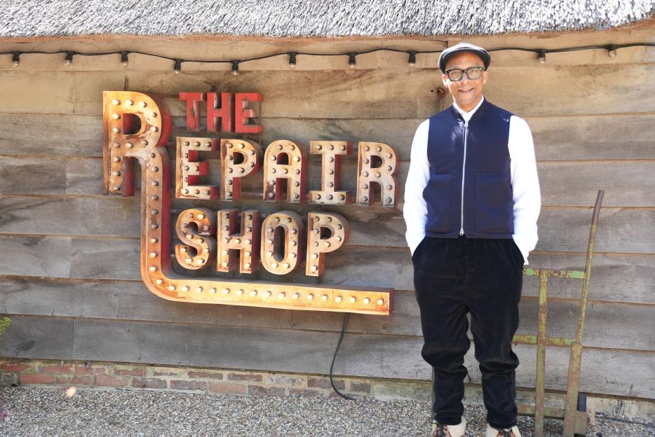 Jay Blades standing in front of The Repair Shop sign.