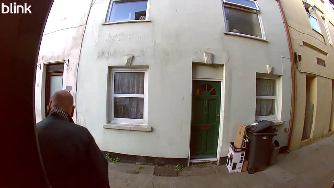Video still of a man defecating on a doorstep.