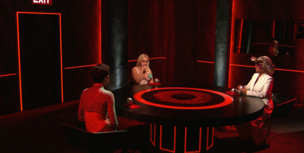 Three women sitting around a round table in a room with red lighting.
