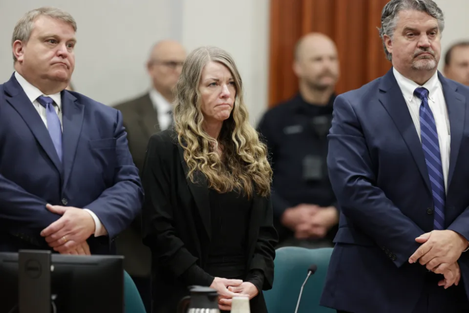 Woman in black jacket flanked by two men in suits during a court proceeding.