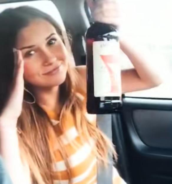 Woman in a car holding a bottle of alcohol.