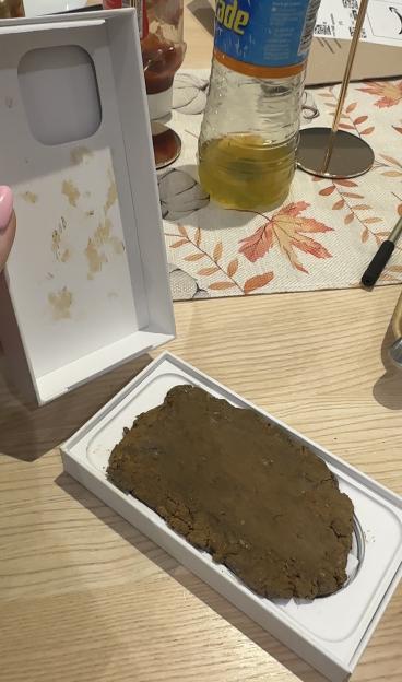 An open iPhone box revealing a brown, mud-like substance inside, next to an empty top box with brown smudges.