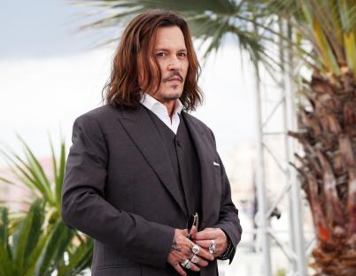a man with long hair and rings on his fingers stands in front of a palm tree