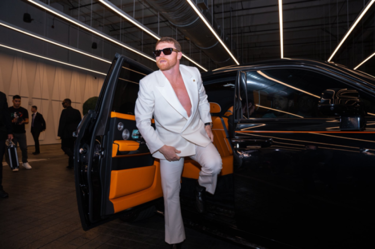 Man in white suit exiting a black car.