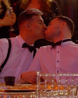 Two men in formal wear kissing.