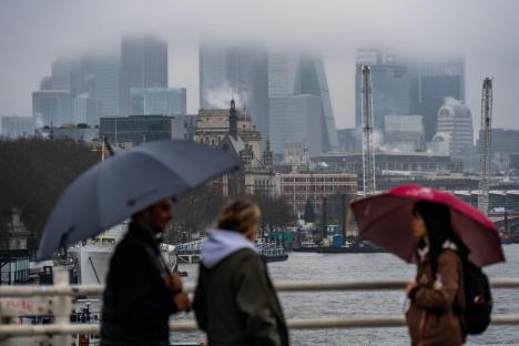 Commuters with umbrellas on a rainy day in London, with the city skyline in the background.