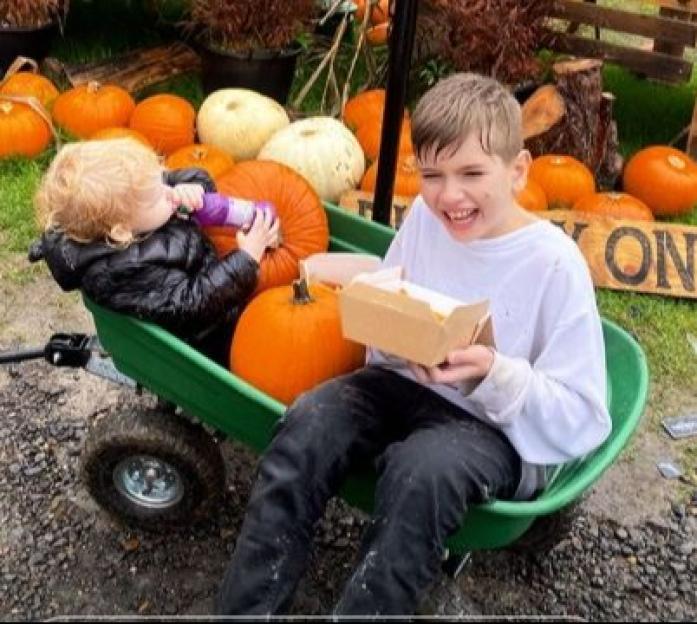 Two young boys playing in a wagon filled with pumpkins at a farm.