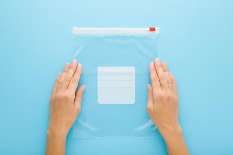 Two hands holding an empty, clear, resealable plastic bag.