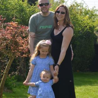 Family portrait of a father, mother, and two young daughters in a garden.