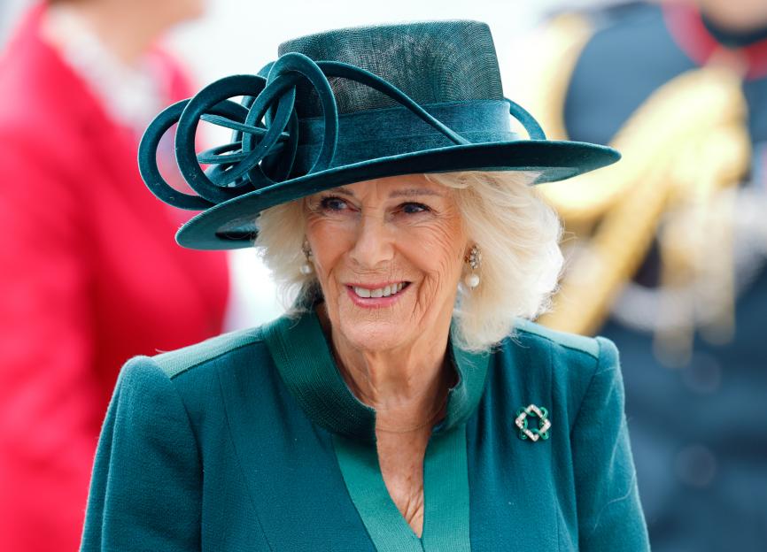 Queen Camilla in a teal dress and hat, smiling at the National Harvest Festival Service.