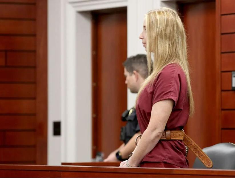 A handcuffed woman stands in a courtroom.