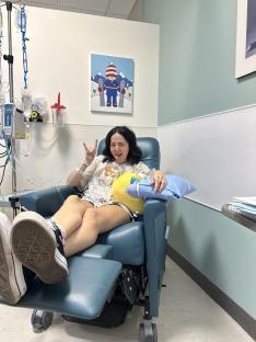 Young woman receiving immunotherapy treatment, giving the rock-on hand gesture.