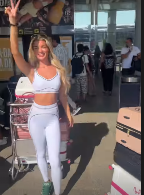 Woman in white athletic wear waves at the airport.