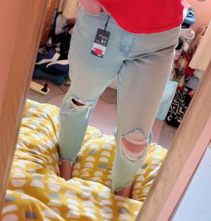 Person in red shirt and ripped jeans taking a selfie in a mirror.