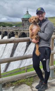 Man holding a dog in front of a dam.