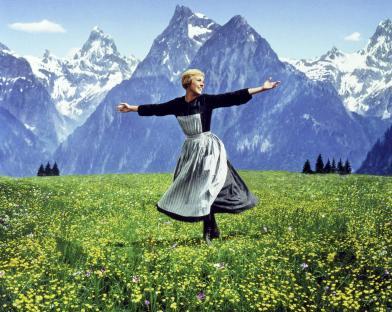 Julie Andrews in The Sound of Music, arms outstretched in a field of flowers with mountains in the background.