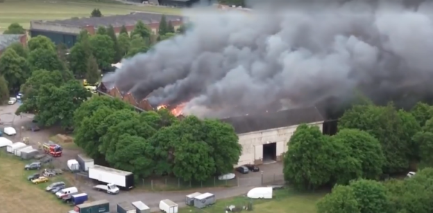 Aerial view of a large building engulfed in flames and thick smoke.