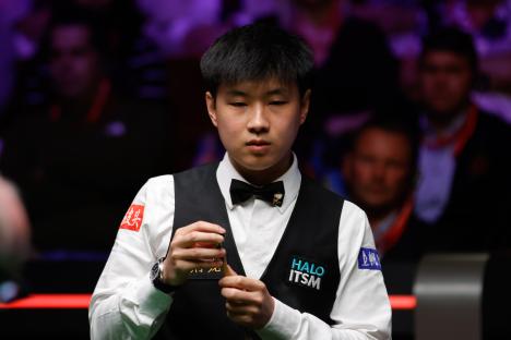 Zhao Xintong chalking his cue during a snooker match.