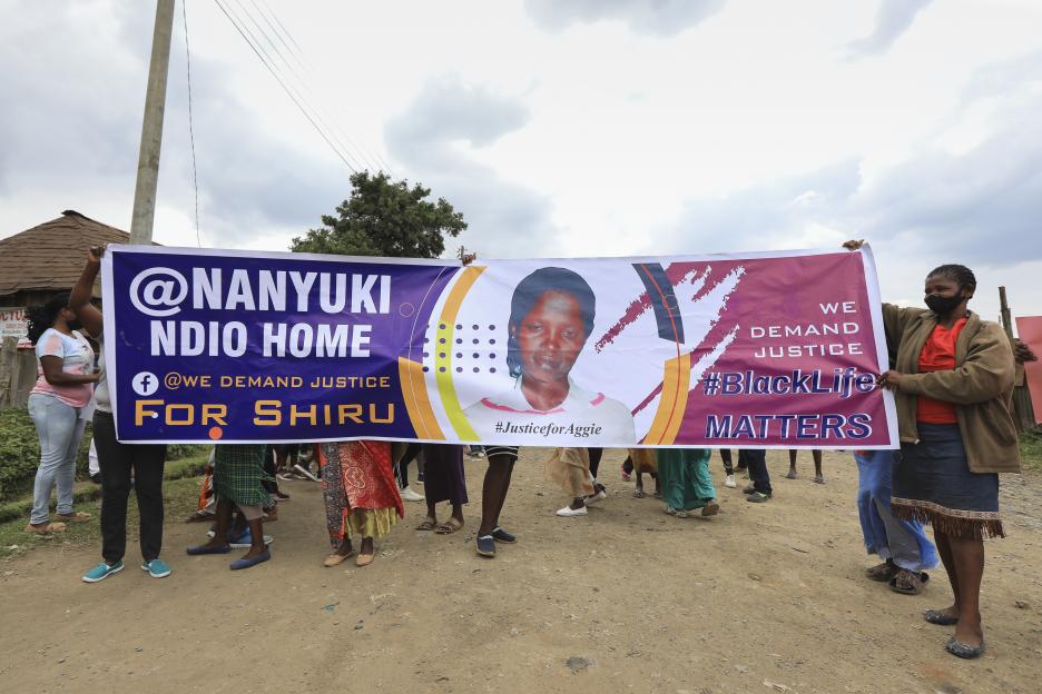 People hold a banner that says "Nanyuki Ndio Home", "We Demand Justice For Shiru", "#JusticeForAggie", "We Demand Justice", and "#BlackLifeMatters", with a picture of Agnes Wanjiru.