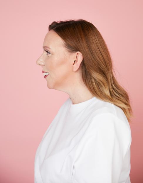Woman in profile view against a pink background.