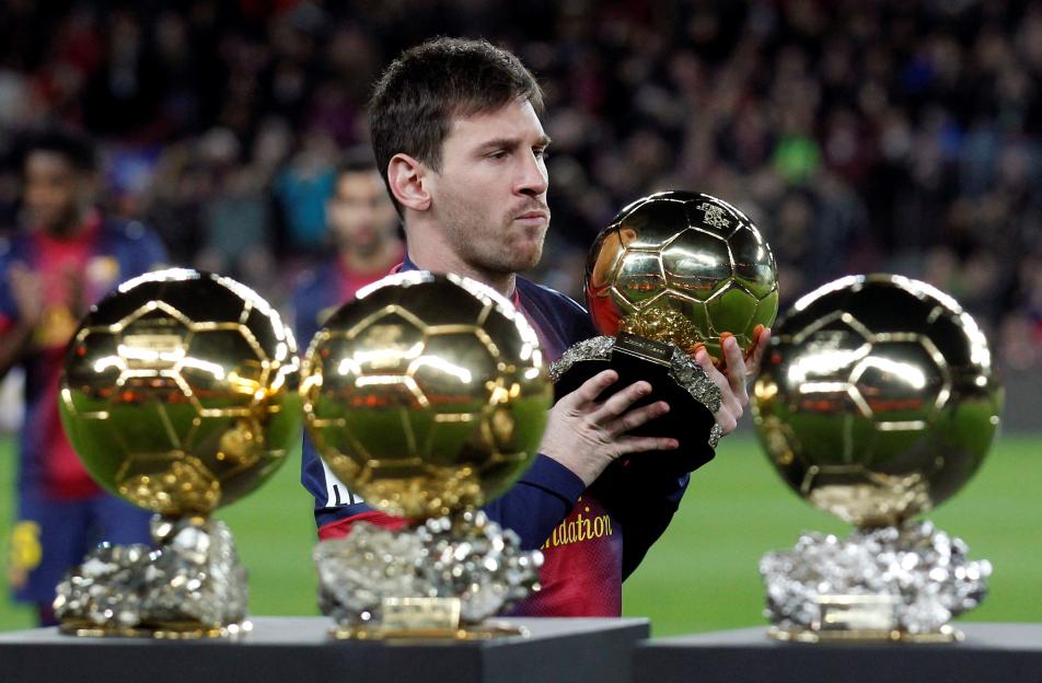Lionel Messi holding four Ballon d'Or trophies.