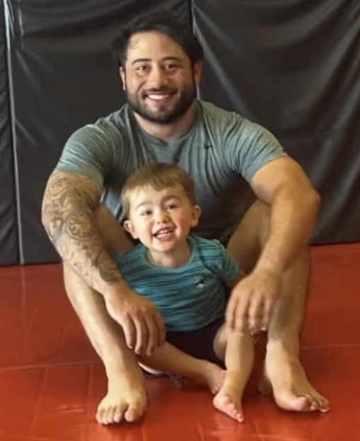 Man with tattooed arm and young child sitting on a red mat.