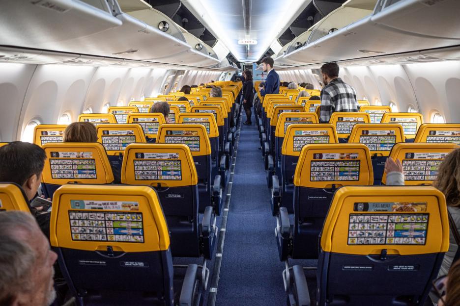 Interior of a Ryanair plane with passengers seated and crew members in the aisle.