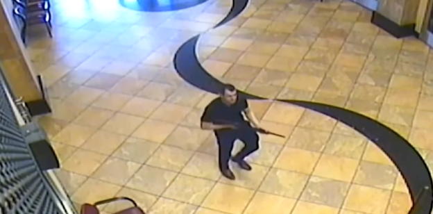 Security camera footage of a man holding a rifle in a building.