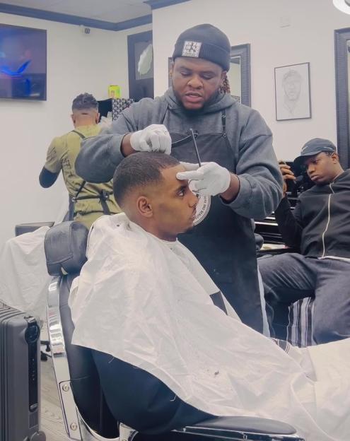 A barber giving a customer a haircut in a salon labeled "Madeinkays barbers & beauty."