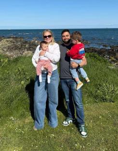 Family photo of parents holding their baby and toddler near the ocean.