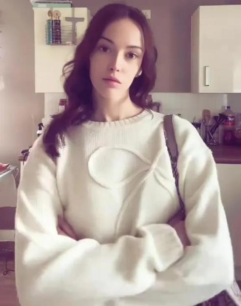 A woman in a white sweater with a decorative tie on the chest asking if the sweater gives off "granny vibes".