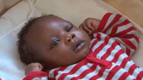Photo of a baby boy lying on his back wearing a red and gray striped outfit.