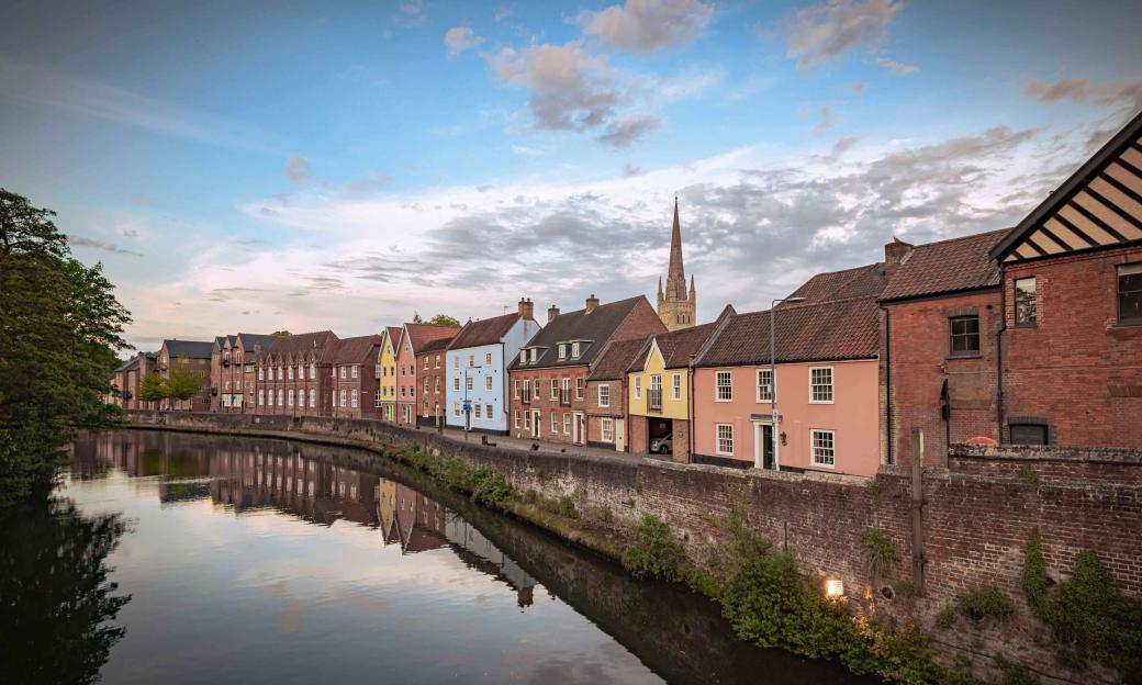 Colorful houses line a river, with a church steeple visible in the background.