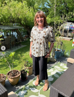 Woman in floral top and black culottes standing on patio.