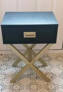 Dark blue bedside table with gold legs and drawer.