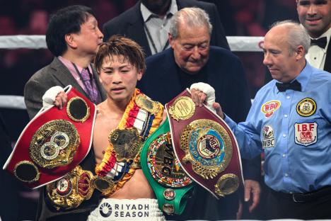 Naoya Inoue holding three boxing championship belts.