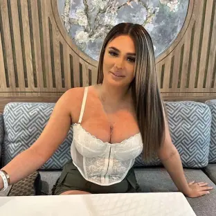 Woman in white lace corset and olive green shorts sitting on a couch.