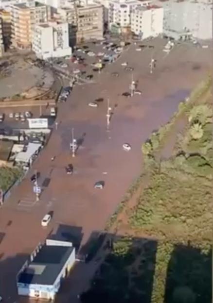 Aerial view of a heavily flooded urban street with cars partially submerged in muddy water.