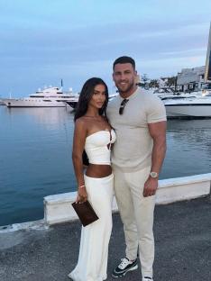 Couple posing by the water in matching white outfits.
