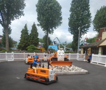 Child driving a Thomas the Tank Engine ride-on tractor at an amusement park.