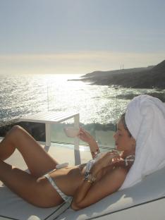 Woman in a bikini relaxing by the ocean with a drink.