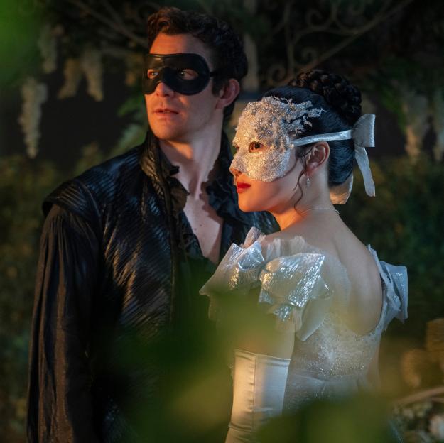 Luke Thompson as Benedict Bridgerton in a black mask and Yerin Ha as Sophie Baek in a white lace mask and a sparkling dress.