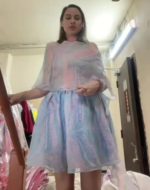 Woman in a short, light blue and pink patterned dress with a sheer, matching shawl, standing on a staircase.