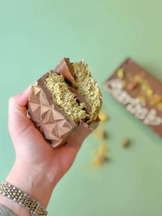 Hand holding a broken piece of Dubai Pistachio and Kunafa chocolate bar.