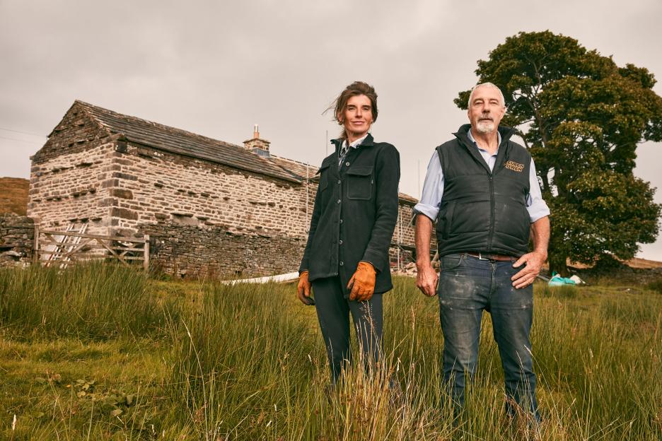 Amanda and Clive Owen standing in front of a stone farmhouse undergoing restoration.