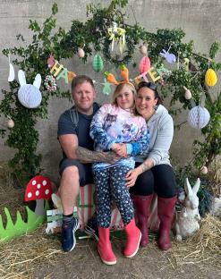 A young girl with her parents in front of an Easter-themed backdrop.